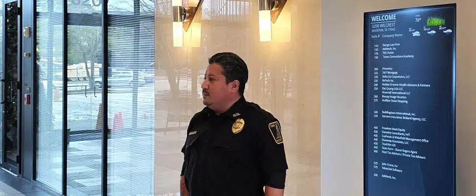 commercial-security-services-kansas-img-1 Security guard standing in office lobby near directory.